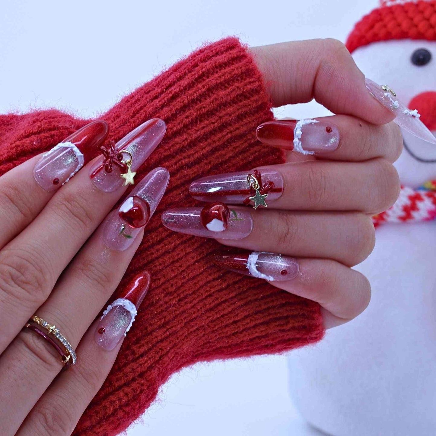 Close-up of hands with festive nail art holding a red knitted item, with a snowman in the background.by Tennail press on nails.