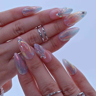 Hand with iridescent nail art and silver rings on a light background by Tennail.