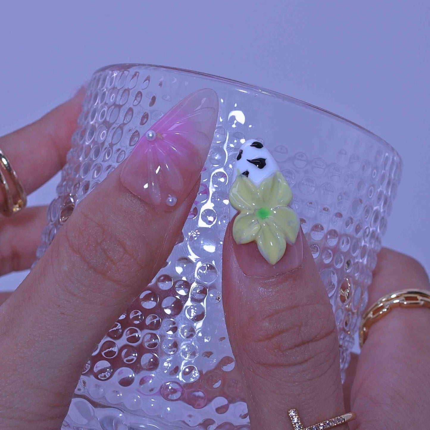 Clear glass with decorative flower charm held by a hand with painted nails , Pastel Floral press on Nails with hand-painted florals, pastel hues, delicate accents by Tennail