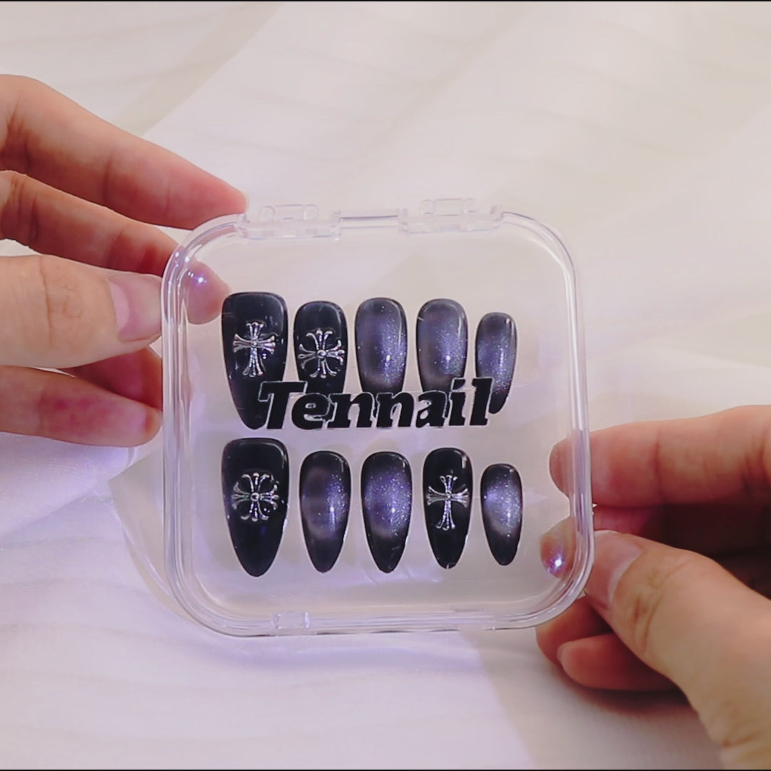 Video shows Nocturne Cross Nails: Edgy short almond press - ons with sleek black cat - eye, gothic cross details catch light as hands move, blending mystery and style—easy to apply for instant vibe elevation.