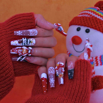 Nails with Christmas-themed designs held by a person wearing red gloves against an orange background by Tennail press on nails.