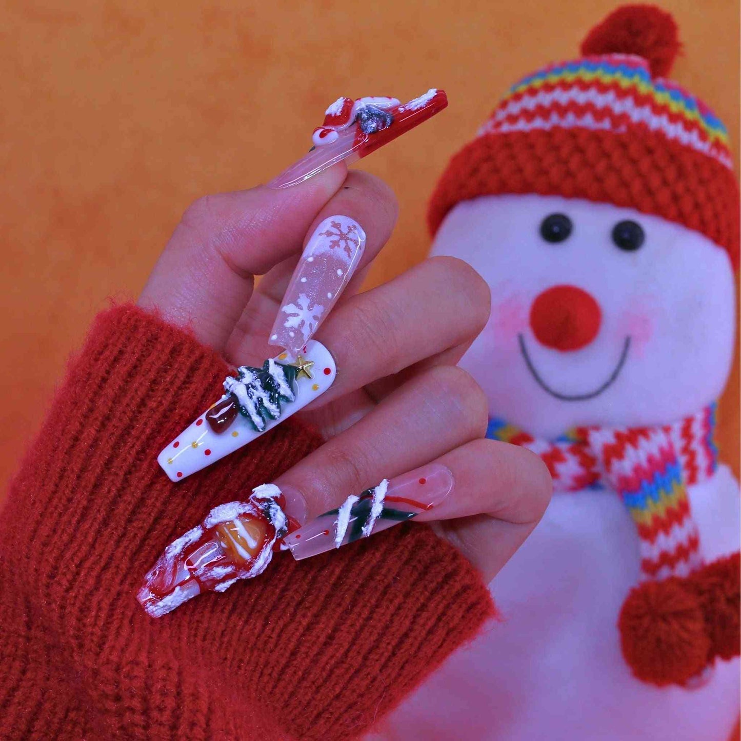 Hand with Christmas-themed nails wearing a red sweater in front of a snowman plush toy. by Tennail press on nails.