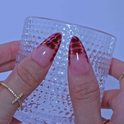 Close-up of hands with red and gold nail art holding a textured glass by Tennail.