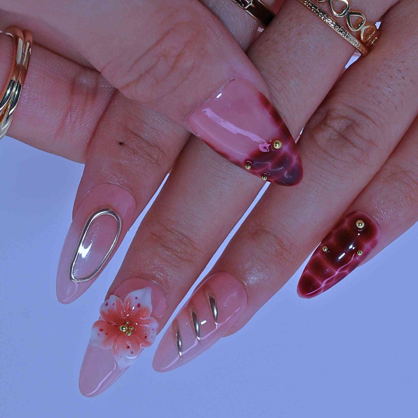 Close-up of hands with pink nail polish and floral designs on a light purple background by Tennail.