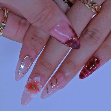 Close-up of hands with pink nail polish and floral designs on a light purple background by Tennail.