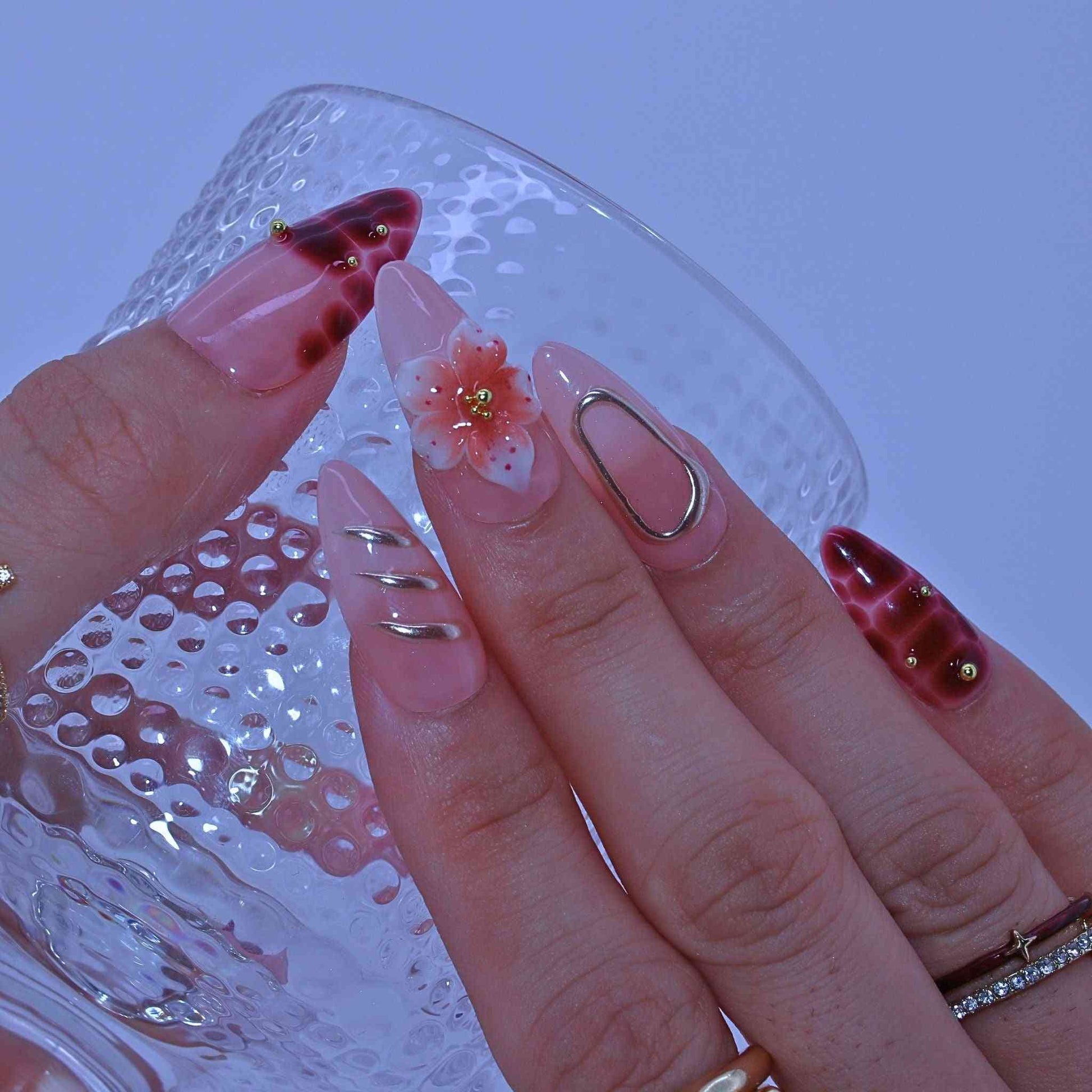 Close-up of a hand with pink and gold nail art holding a glass with water by Tennail.droplets.