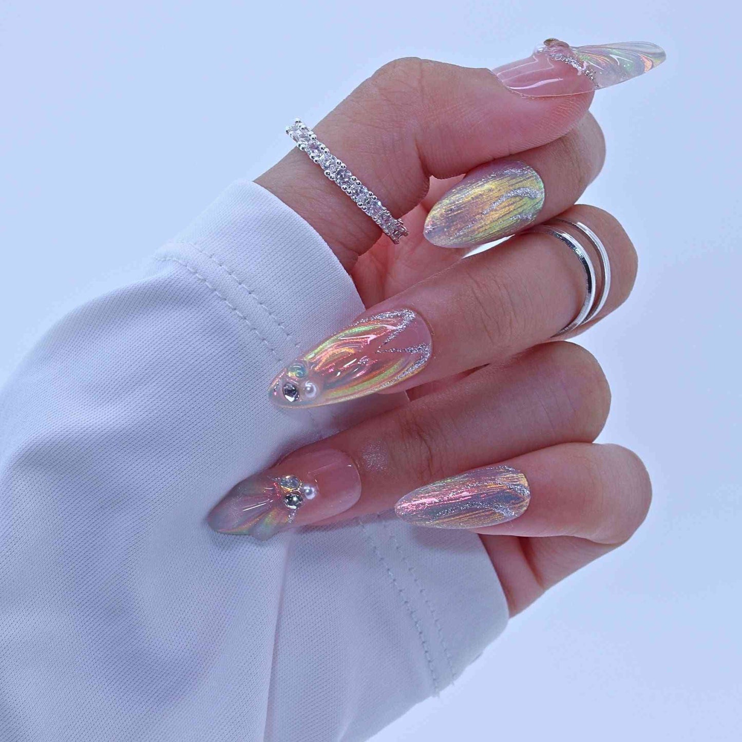 Hand with iridescent nail art and rings on a light blue background by Tennail.