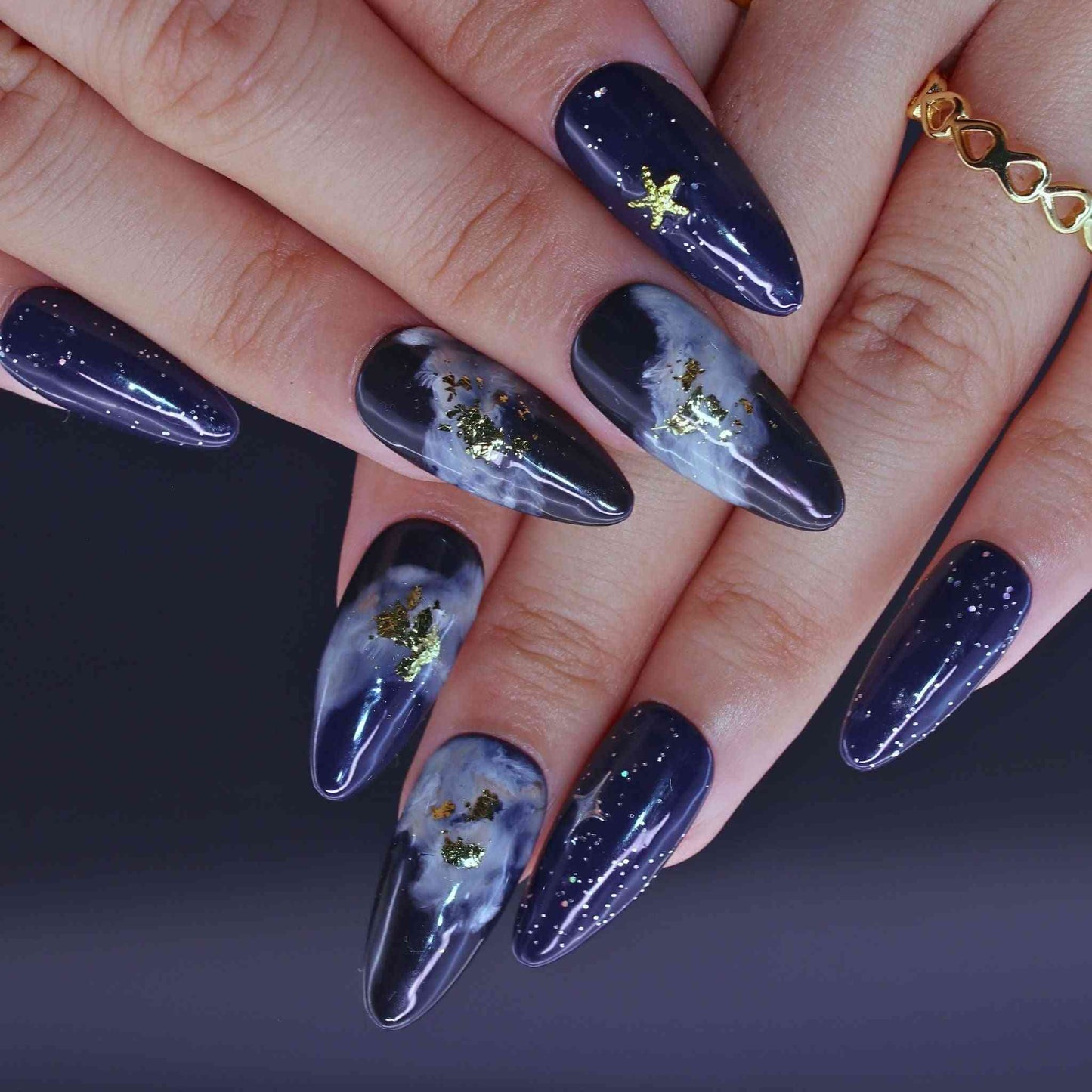 Nails with dark blue nail polish and gold star decorations by Tennail.