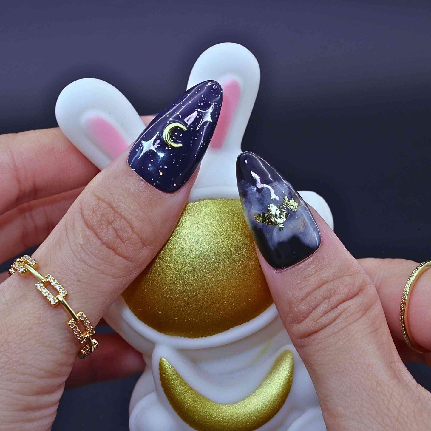Nails with galaxy design held by a person wearing bunny-shaped nail by Tennail.polish holder.