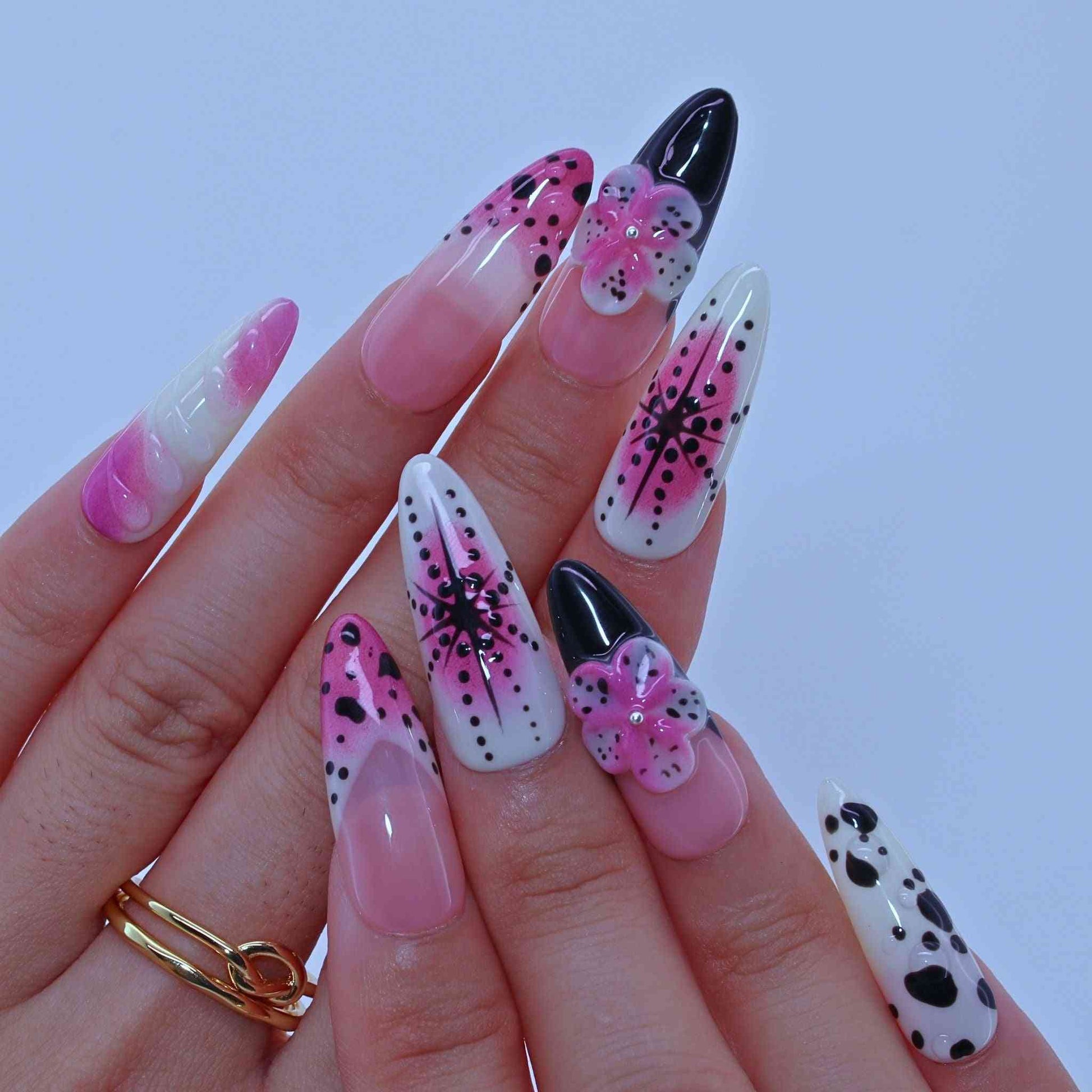 Hand with long, stylishly designed nails featuring pink, black,Dotted Blossom Nails with black dots, purple florals, hand-painted art by Tennail
