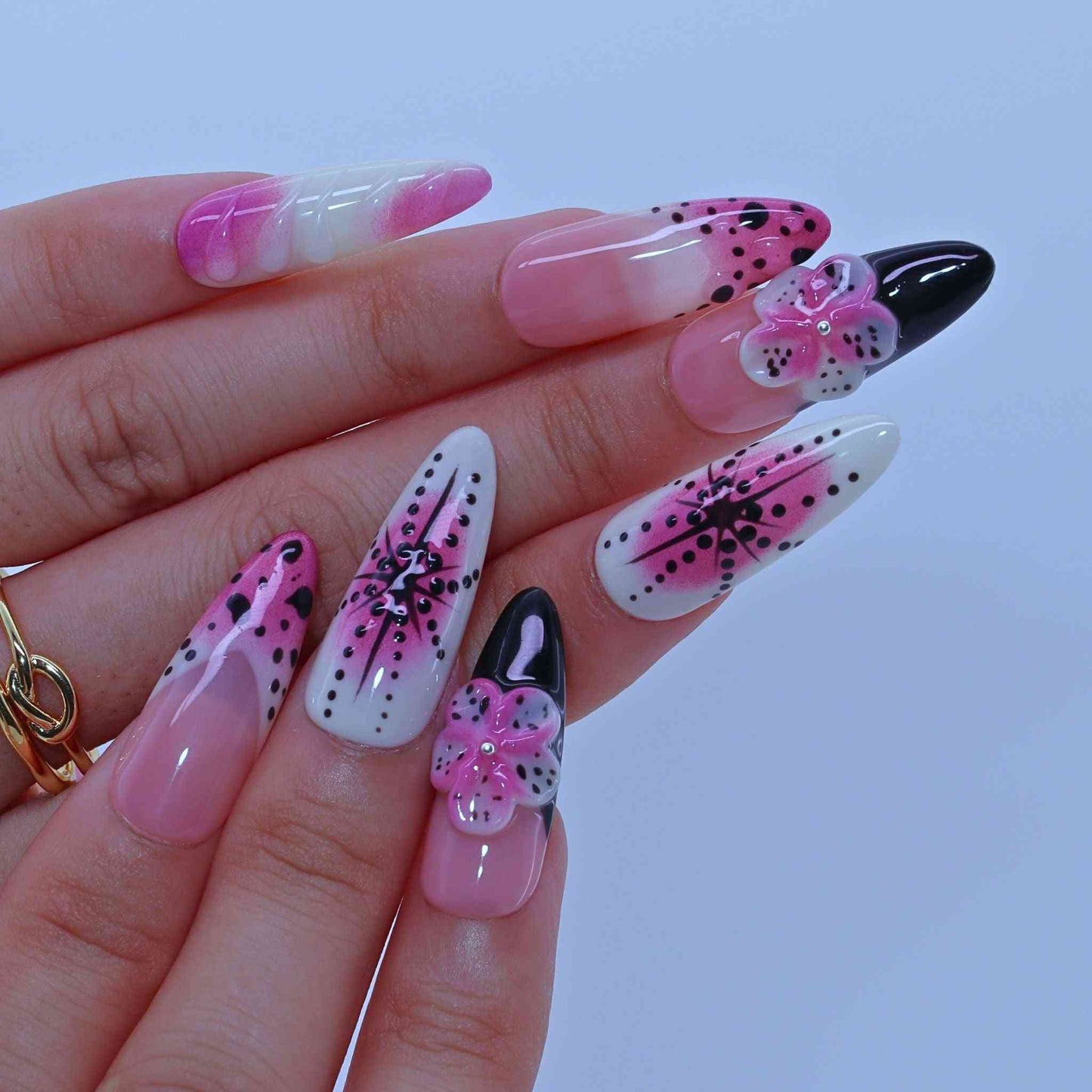 Hand with long, intricately designed nails featuring pink, black, Dotted Blossom Nails with black dots, purple florals, hand-painted art by Tennail