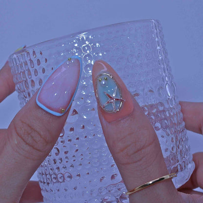 Close-up of a hand with decorative nails holding a textured glass , Coastal Bloom press on Nails with hand-painted florals, starfish accents, coastal hues by Tennial