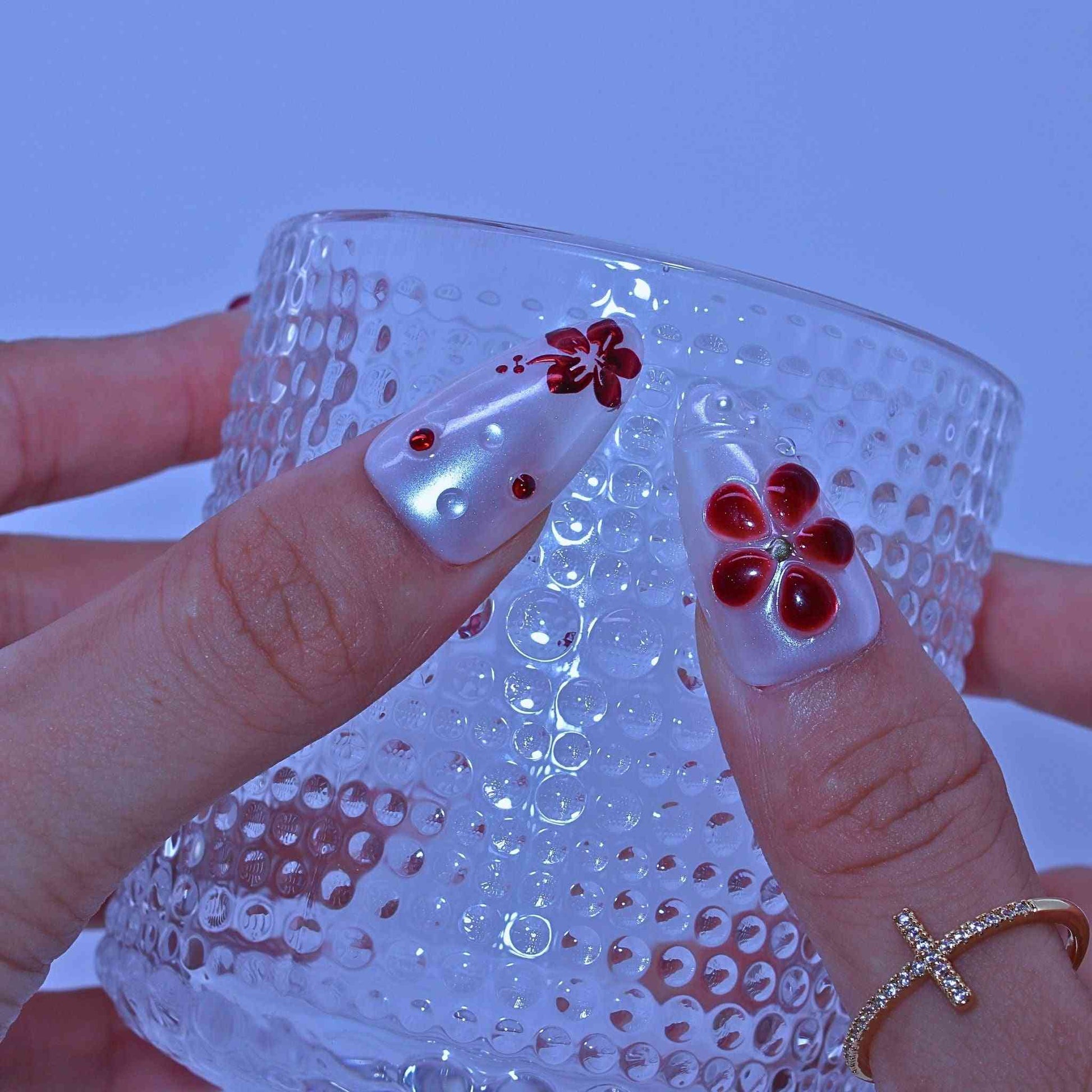 Clear glass with textured surface held by a hand with red flower nail art , Crimson Bloom press on Nails with hand-painted red florals, gradients, rhinestone accents by Tennail