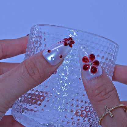 Clear glass with textured surface held by a hand with red flower nail art , Crimson Bloom press on Nails with hand-painted red florals, gradients, rhinestone accents by Tennail