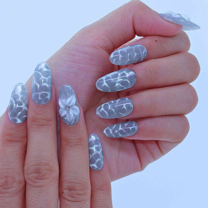Hand with decorative silver nail art, Aqua Wave press on Nails with hand-painted waves, aqua cat-eye, floral accents by Tennail.