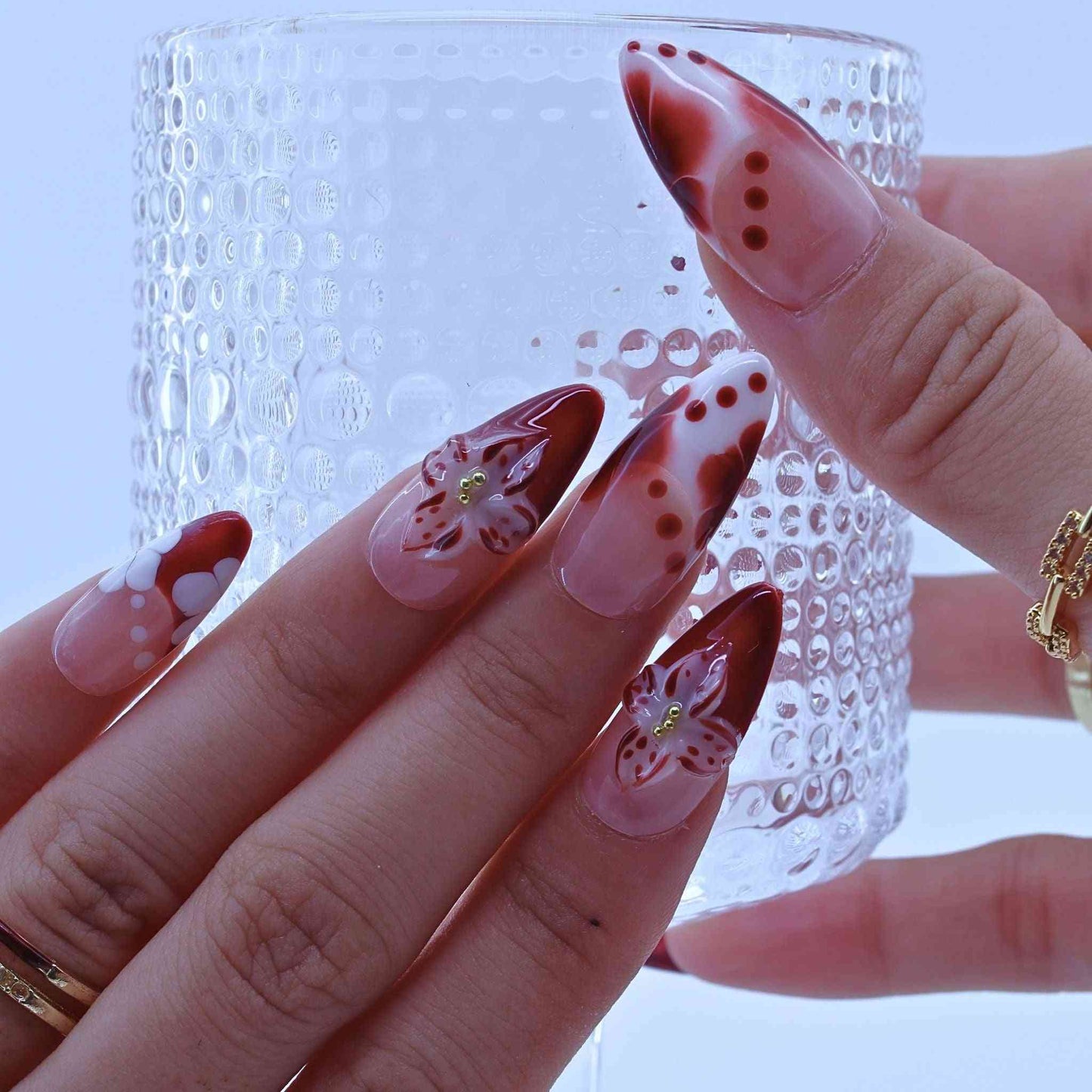 Close-up of a hand with decorative nail art, Tropical Flowers Press on Nails with hand-painted florals, red gradients, delicate accents by Tennail.