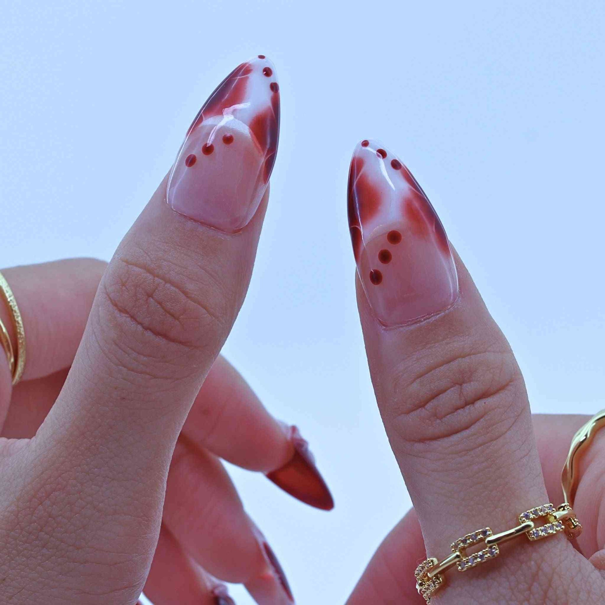Close-up of a hand with marbled red and pink nail polish, Tropical Flowers Press on Nails with hand-painted florals, red gradients, delicate accents by Tennail.