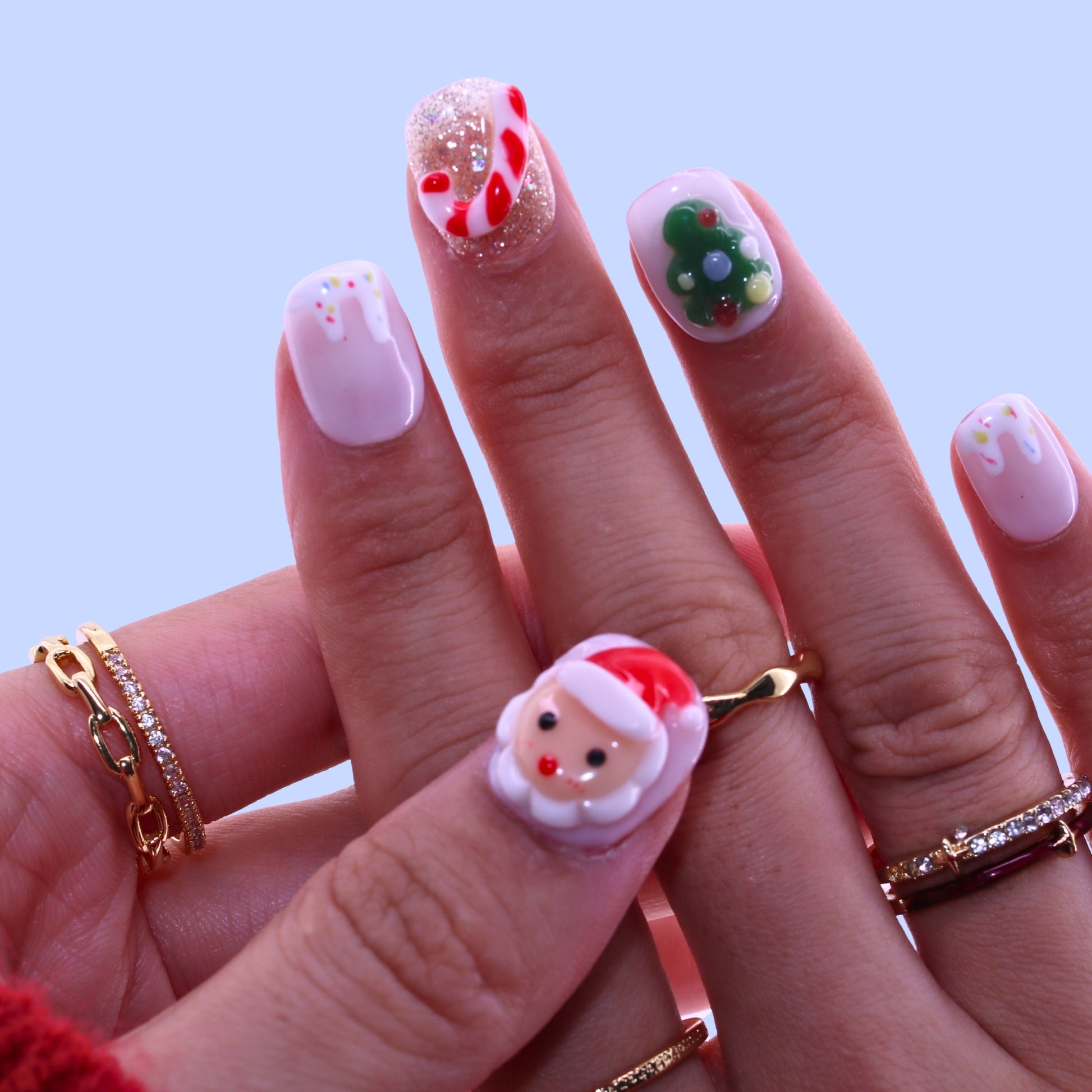 Close-up of a hand with festive nail art featuring Santa Claus designs on a light blue background, Tennail handmade press on nails.