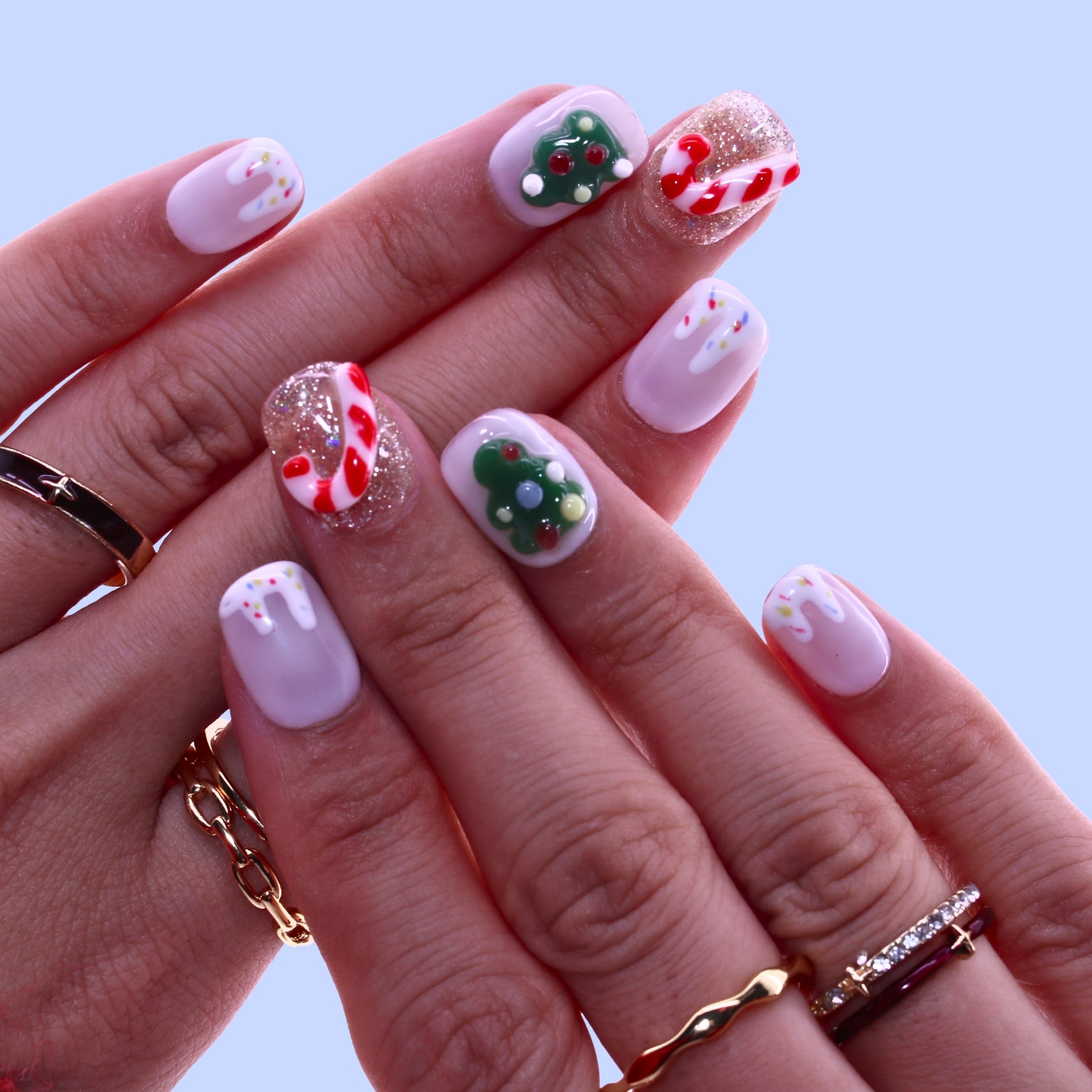 Hand with Christmas-themed nail art on a light blue background, Tennail handmade press on nails