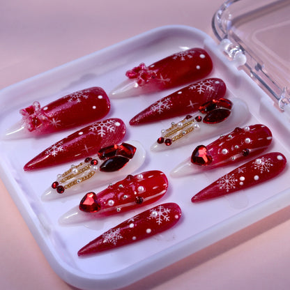 Long Stiletto Christmas press-on nails with red glitter, rhinestones, and snowflakes.