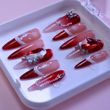 Long Stiletto Christmas press-on nails with red Ombré glitter, 3D bows, and painted snowflakes.