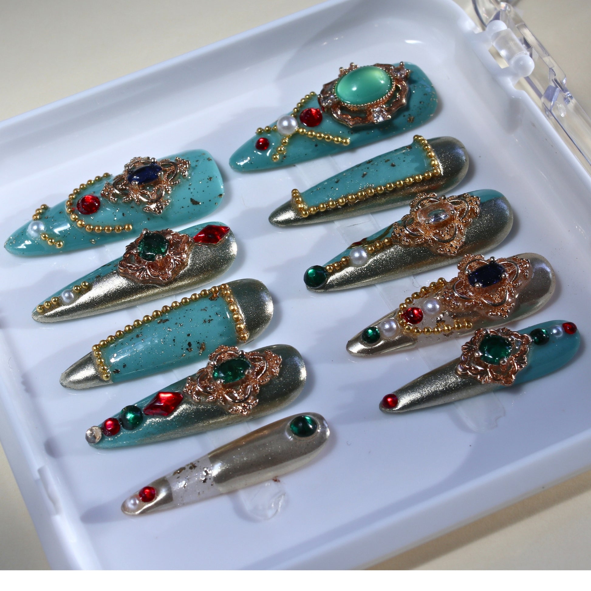 Long Stiletto press-on nails in turquoise and metallic gold with multi-colored rhinestones and pearls.