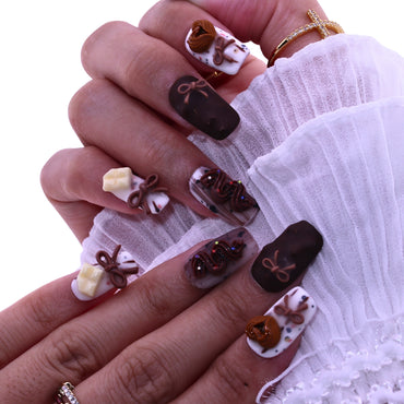 Close-up of a hand with intricately designed nails featuring chocolate-themed decorations, Tennail handmade press on nails.