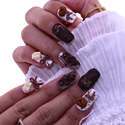 Close-up of a hand with intricately designed nails featuring chocolate-themed decorations, Tennail handmade press on nails.